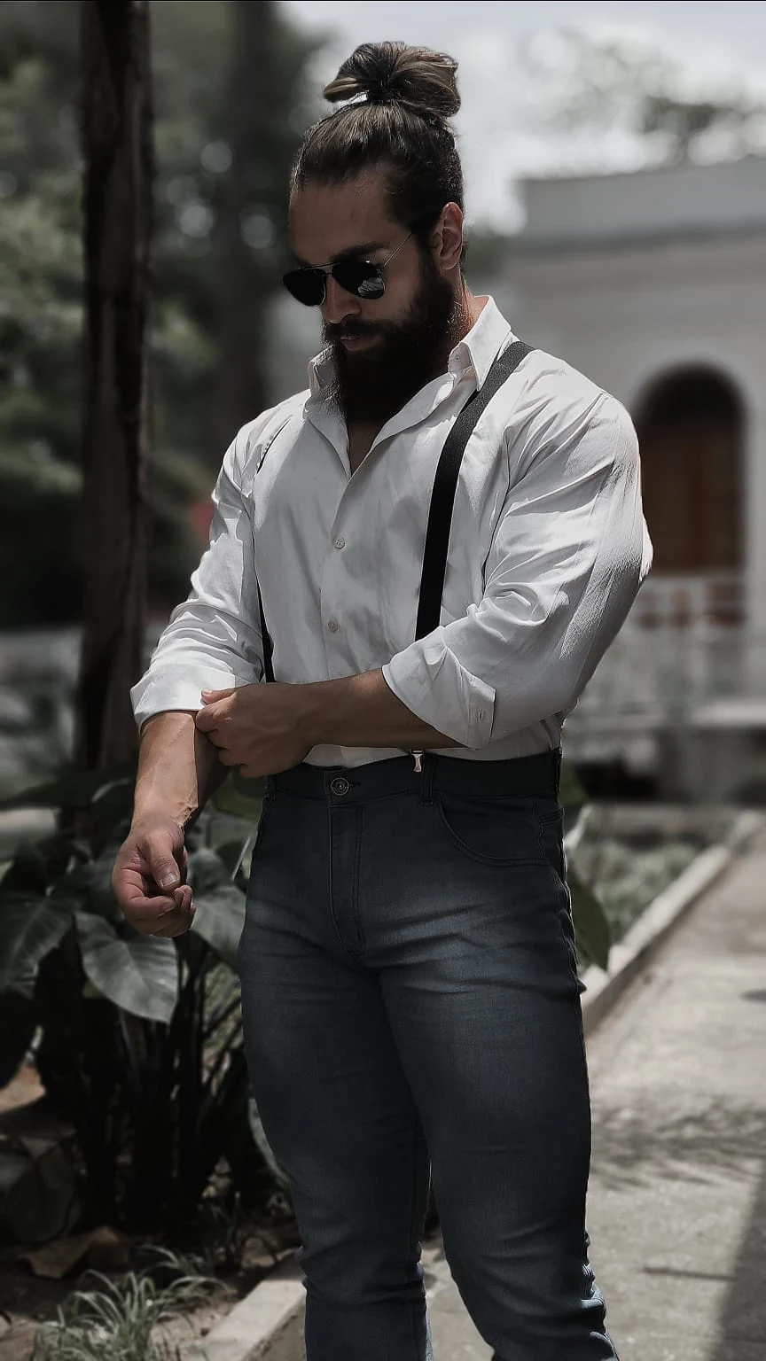 Aron Girardelli em ensaio editorial de corpo inteiro, vestindo camisa branca e suspensórios